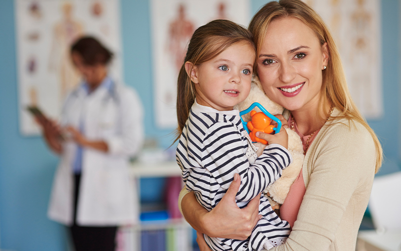 Woman holding child; healthcare provider in background