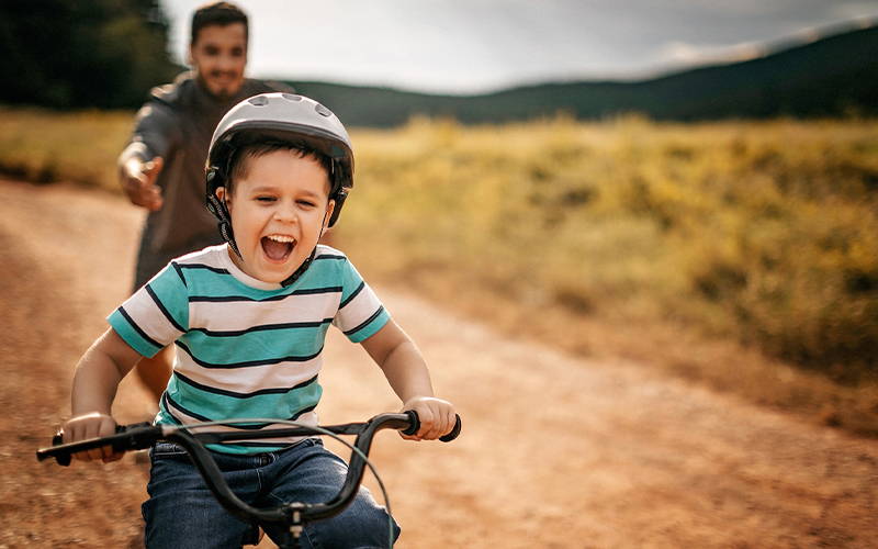 Young child in helmet riding bicycle with adult in background