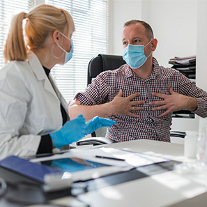 masked man talking with a doctor and gesturing to his chest